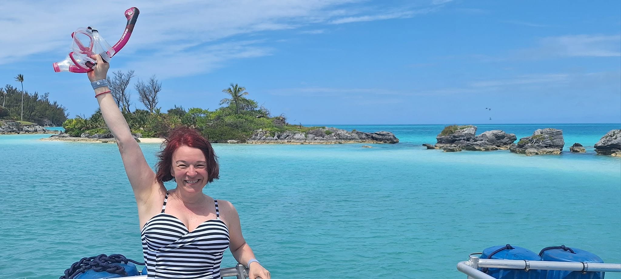 Edina holding her snorkeling gear beside brilliant turquoise water