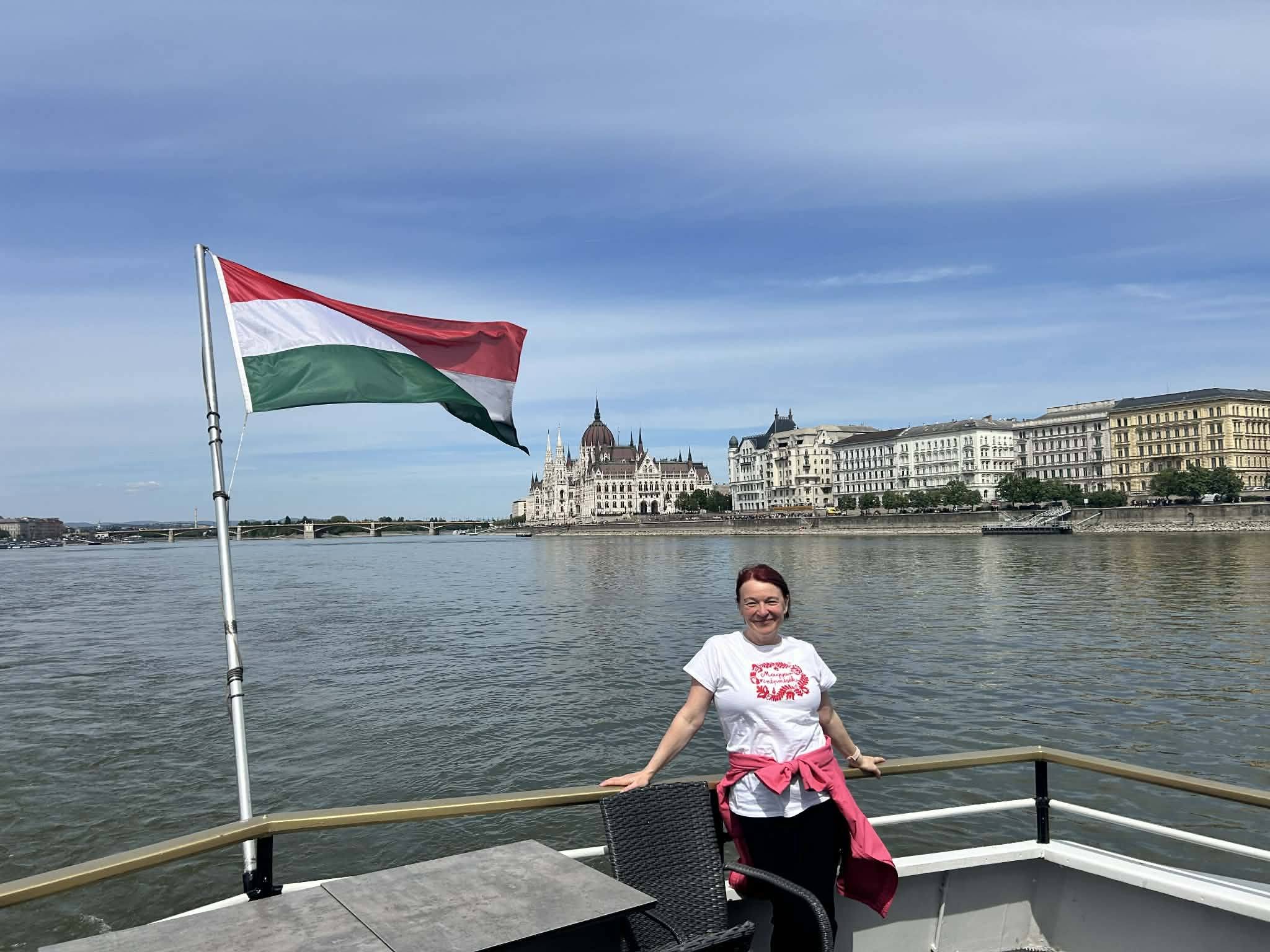 Edina aboard a river cruise in Budapest with the Hungarian flag and Parliament behind her